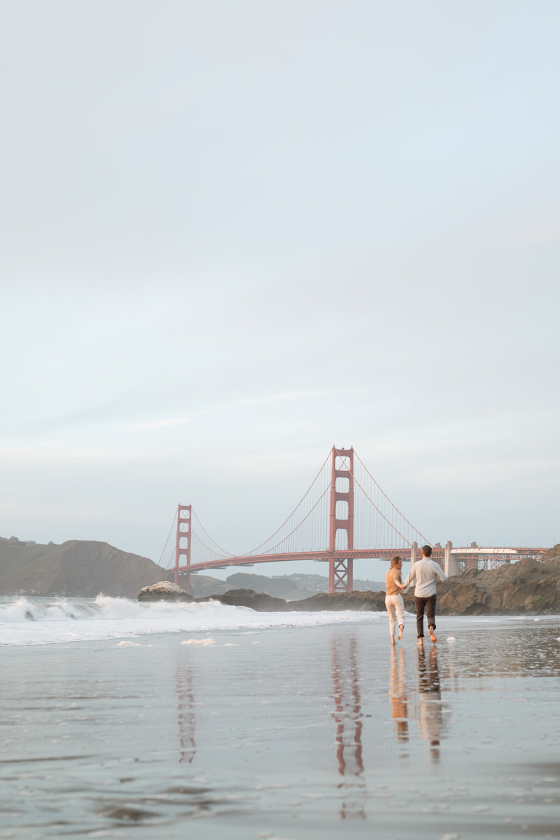 Newly engaged couple running towards the Golden Gate Bridge