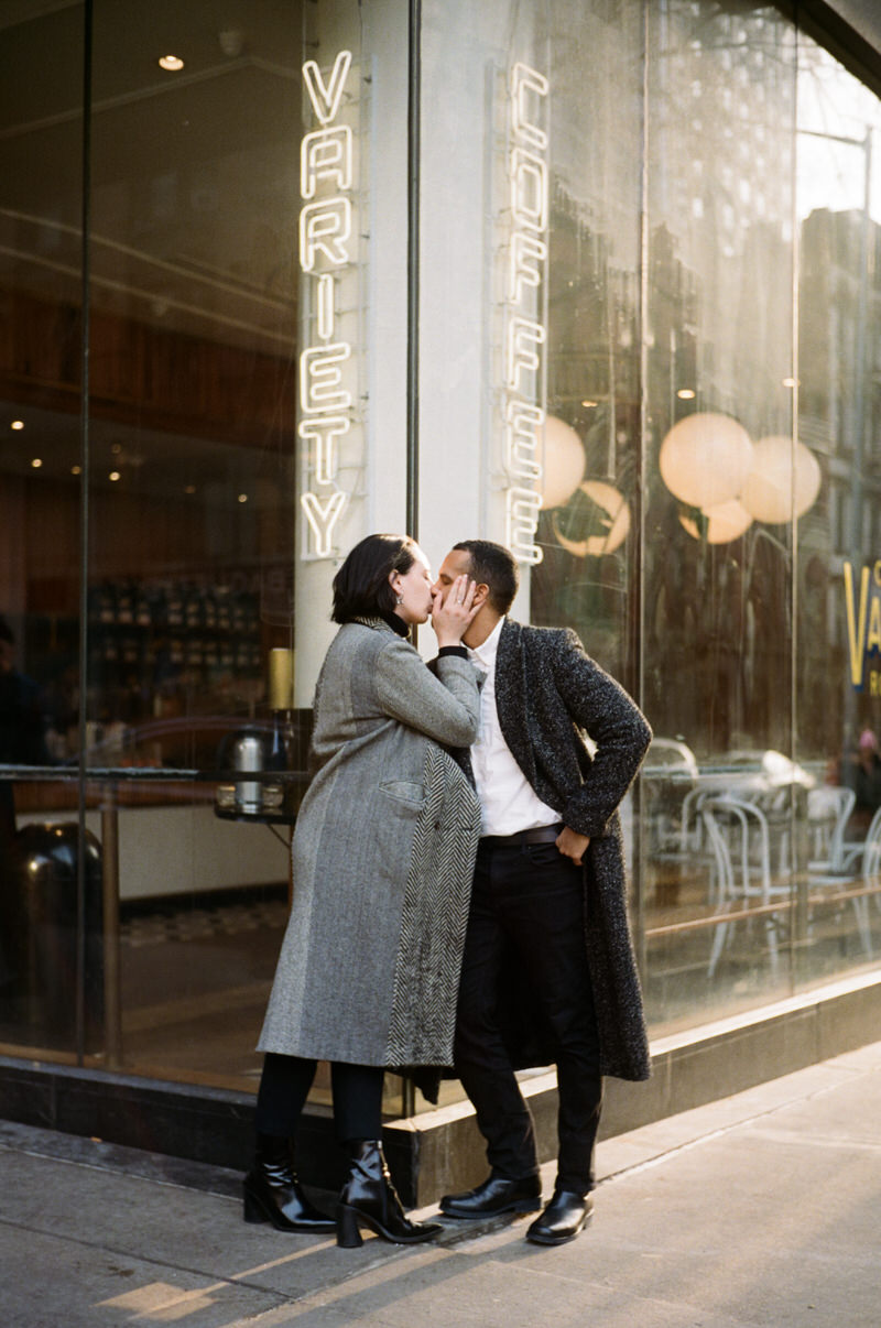Couple kissing outside Variety Coffee Roasters neon sign during NYC film engagement session